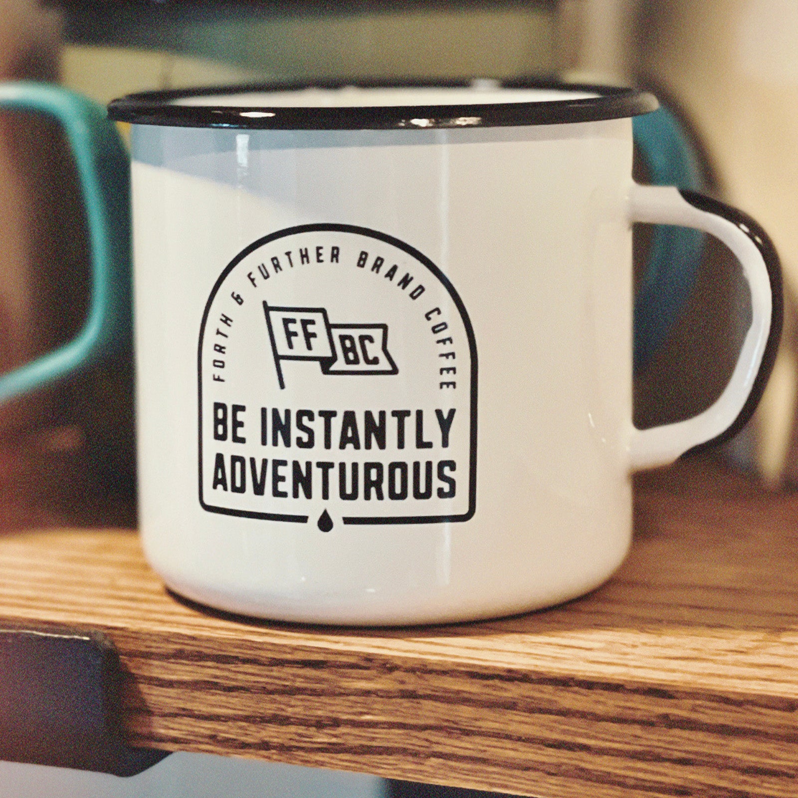 White enamel camp mug with black text and branding on a wooden surface