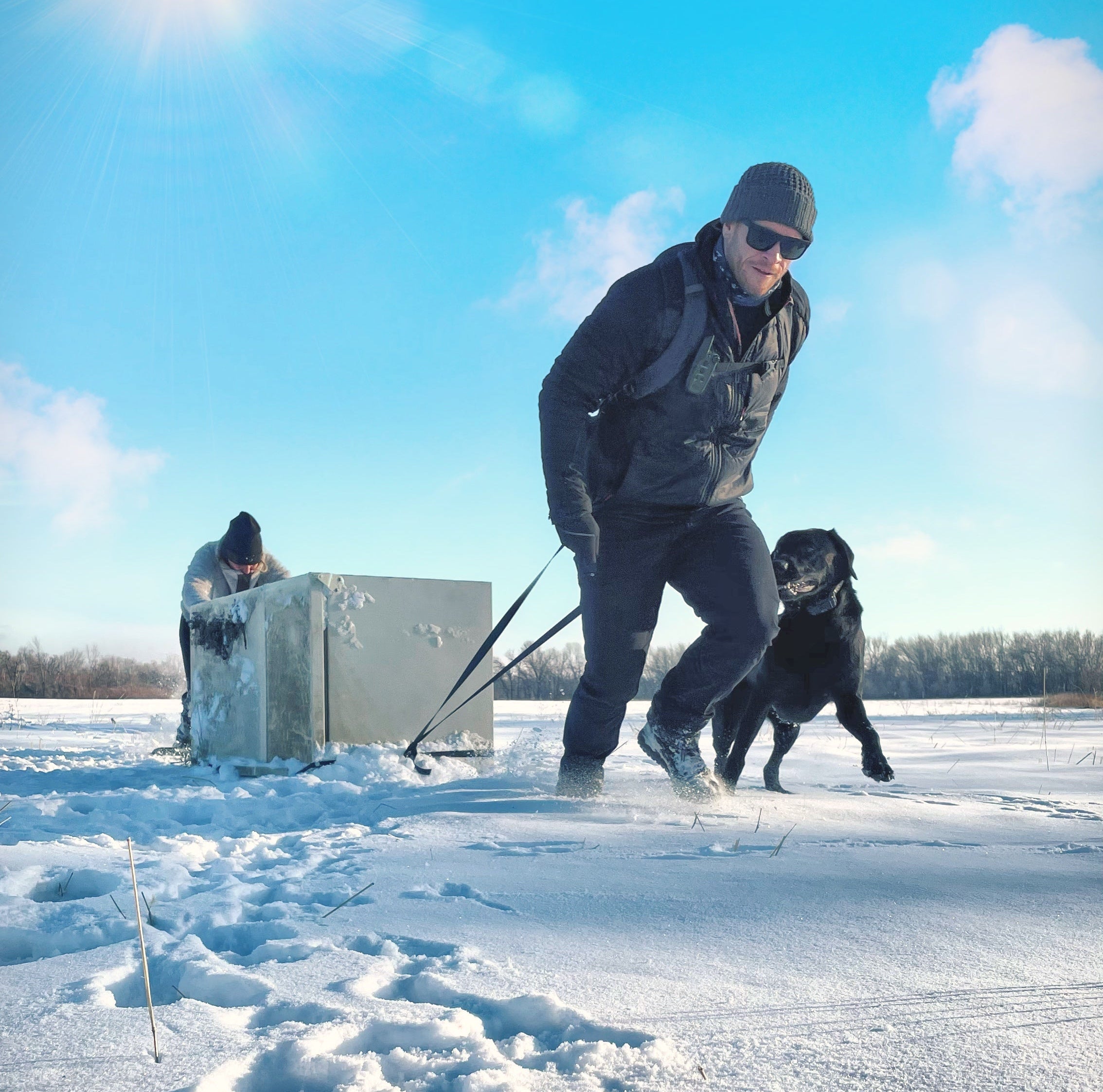 Person dragging an abandoned refrigerator from the wild with a dog.
