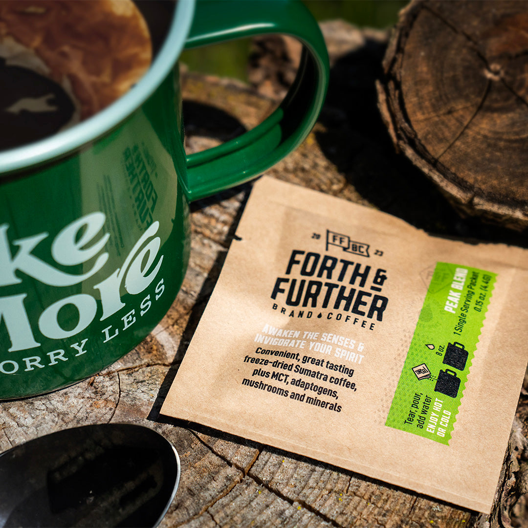 Forth & Further compostable coffee packaging and green camp mug with 'Hike More, Worry Less' text, wooden background