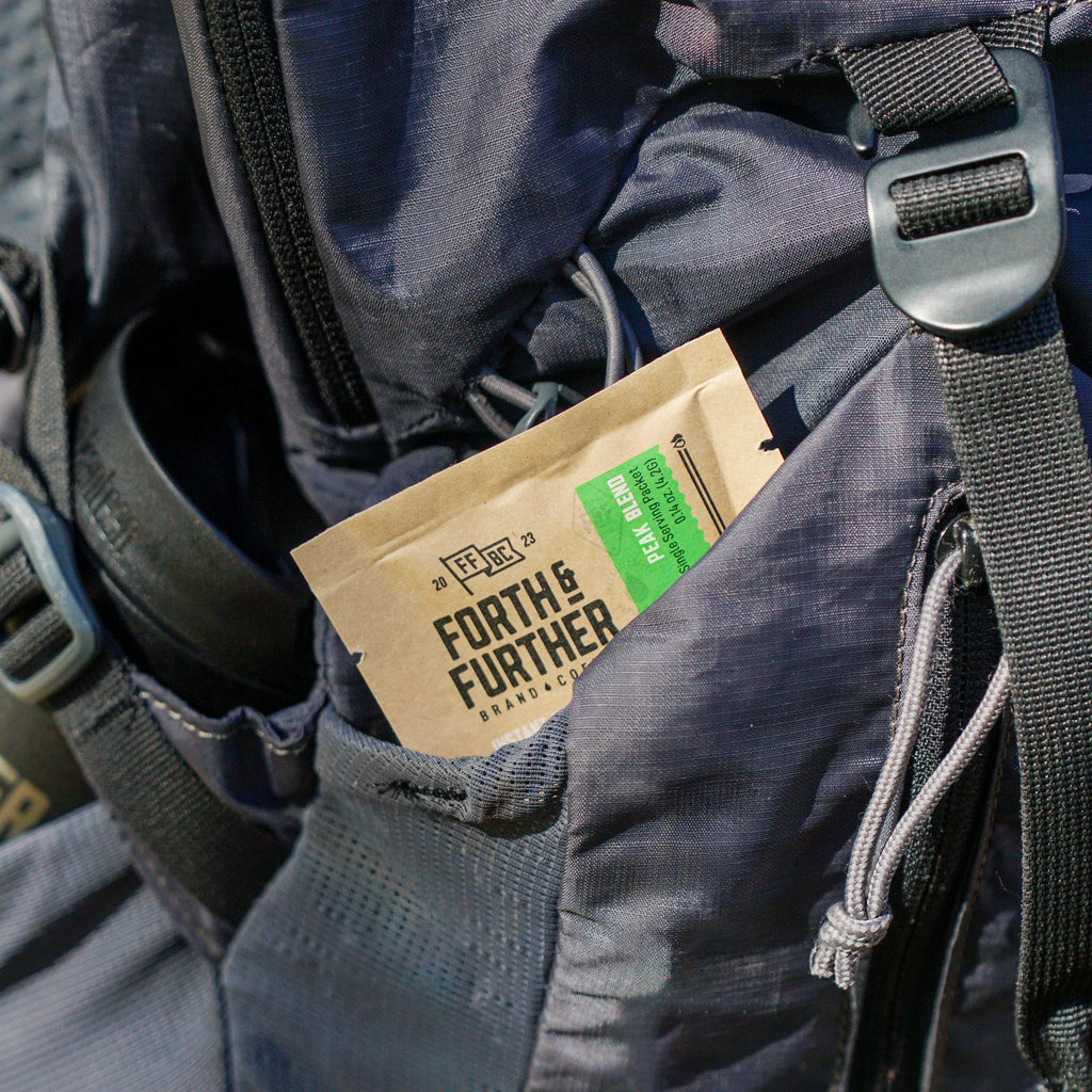 Close-up of a backpack with a Forth & Further coffee packet inside, on a natural background.